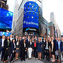 A large group of people standing in front of a Tradeweb marquee in the downtown of a city
